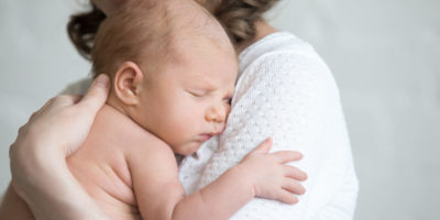 Newborn babe napping on woman arms. Young happy mother tenderly hugging sleeping adorable healthy new born child. Focus on little kid. Love, bonding, happy family concept. Close-up portrait