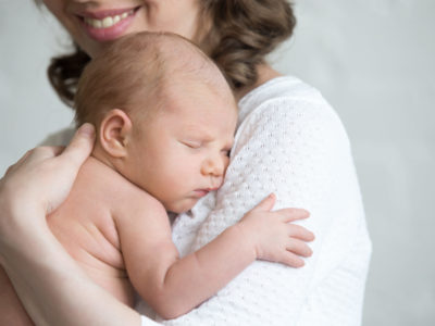 Newborn babe napping on woman arms. Young happy mother tenderly hugging sleeping adorable healthy new born child. Focus on little kid. Love, bonding, happy family concept. Close-up portrait