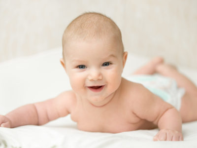 Funny infant baby at home, holds head up, put on a tummy on a white blanket. Family, baby development concept photo