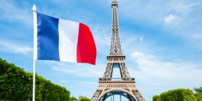 French flag flying in bright blue sky above the Eiffel Tower in