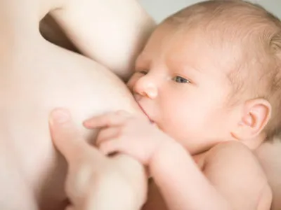 Close-up portrait of sweet newborn baby breastfeeding. Young mother holding her baby on her arms feeding. Happy motherhood concept, indoors shot