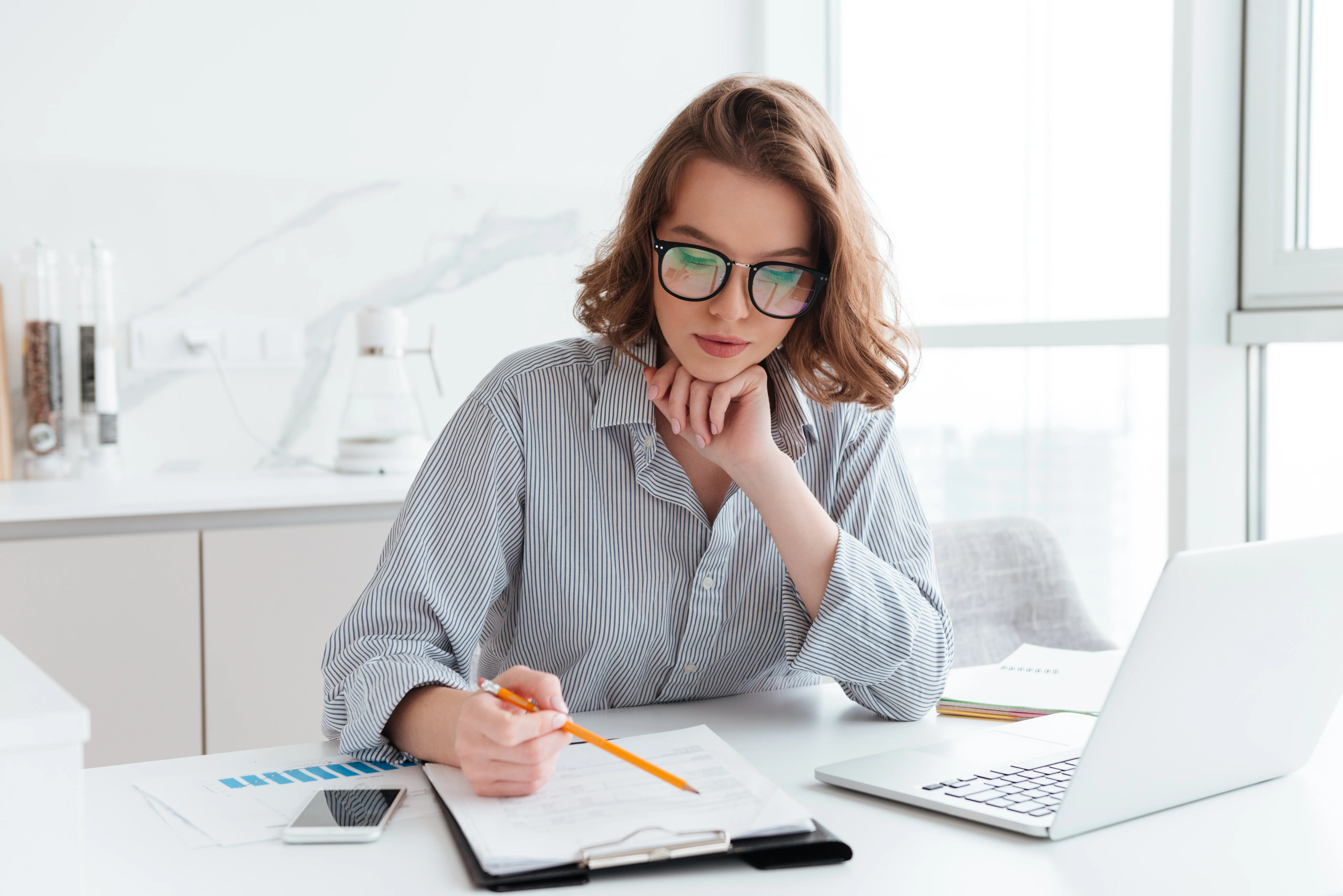 Young concentrated businesswoman in glasses and striped shirt wo